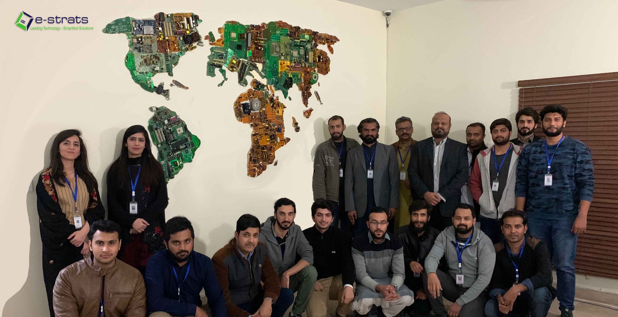 team of e-strats IT company posing infront of a world map made out of e-scrap